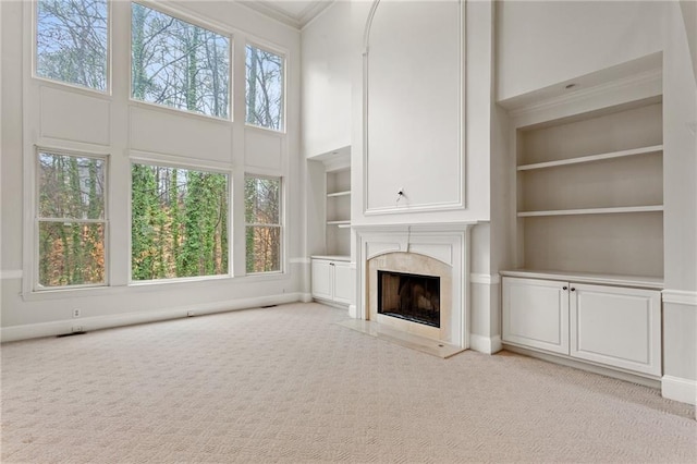 unfurnished living room featuring light carpet, built in shelves, crown molding, a premium fireplace, and a towering ceiling