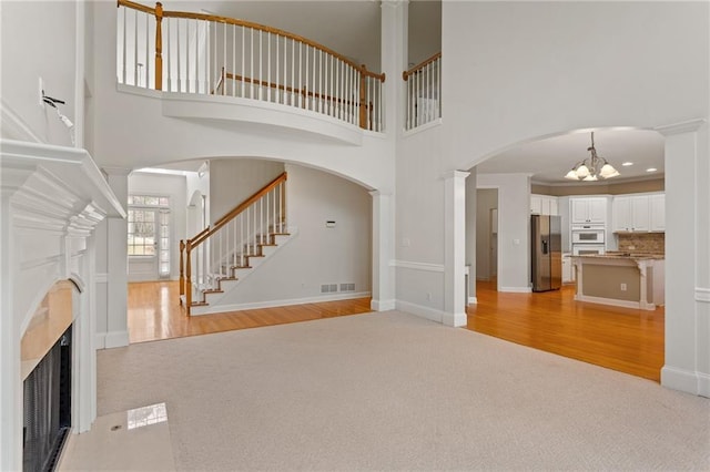 unfurnished living room featuring a fireplace with flush hearth, stairway, light wood-style floors, an inviting chandelier, and light colored carpet