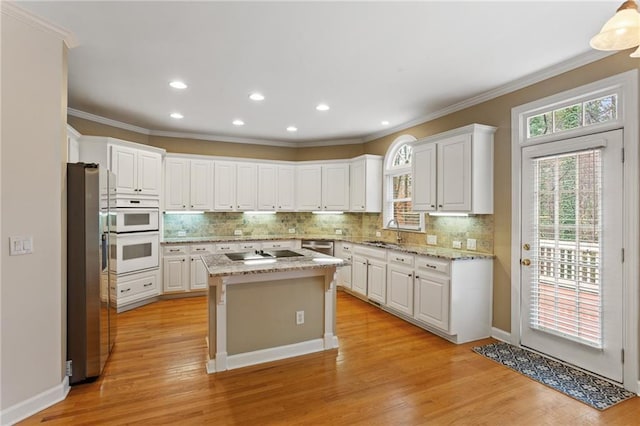 kitchen featuring backsplash, white cabinetry, stainless steel appliances, light wood-style floors, and crown molding