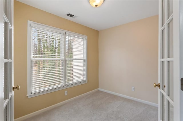 carpeted spare room featuring plenty of natural light, baseboards, visible vents, and french doors