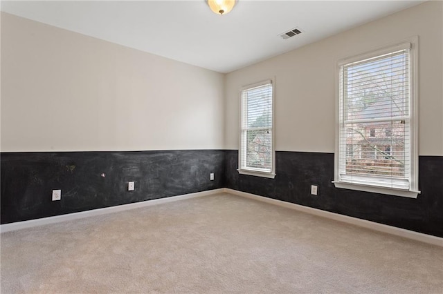 carpeted spare room featuring baseboards, visible vents, and wainscoting