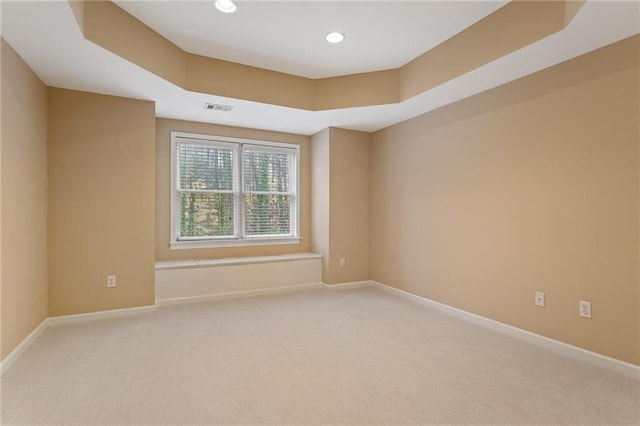 spare room with light carpet, recessed lighting, a tray ceiling, and baseboards