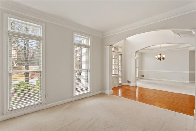 carpeted empty room featuring wood finished floors, baseboards, an inviting chandelier, arched walkways, and crown molding