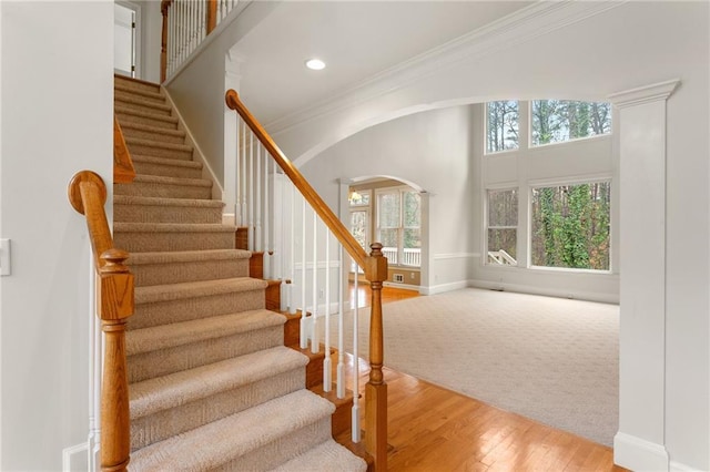 stairs with baseboards, ornamental molding, a towering ceiling, wood finished floors, and arched walkways