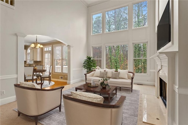 living room featuring arched walkways, a high ceiling, an inviting chandelier, crown molding, and a premium fireplace