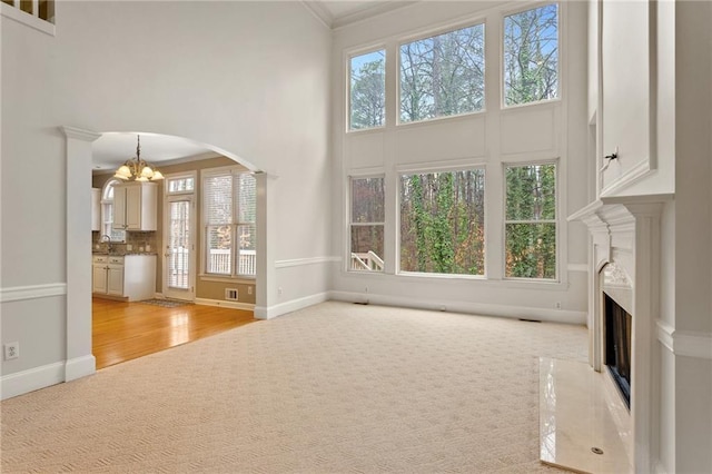 unfurnished living room with plenty of natural light, light colored carpet, an inviting chandelier, and a fireplace