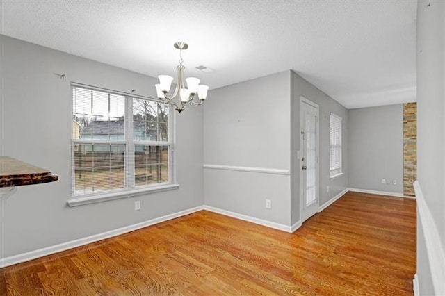 unfurnished dining area with an inviting chandelier, wood finished floors, baseboards, and a textured ceiling