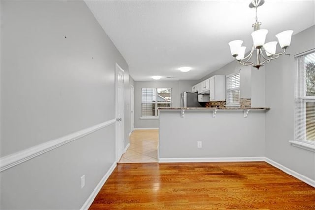 kitchen featuring a kitchen bar, light wood-style flooring, a peninsula, freestanding refrigerator, and a notable chandelier