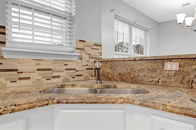 kitchen with a notable chandelier, a sink, white cabinetry, decorative backsplash, and light stone countertops