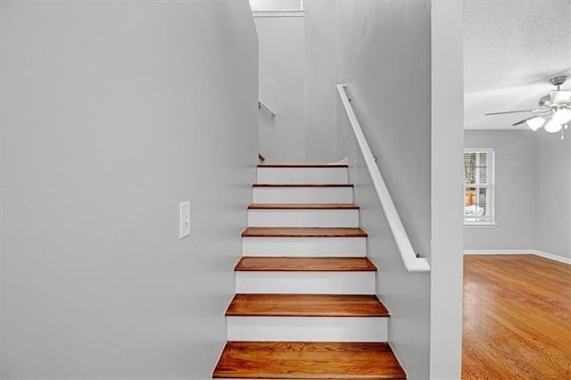 stairway featuring a textured ceiling, wood finished floors, baseboards, and ceiling fan