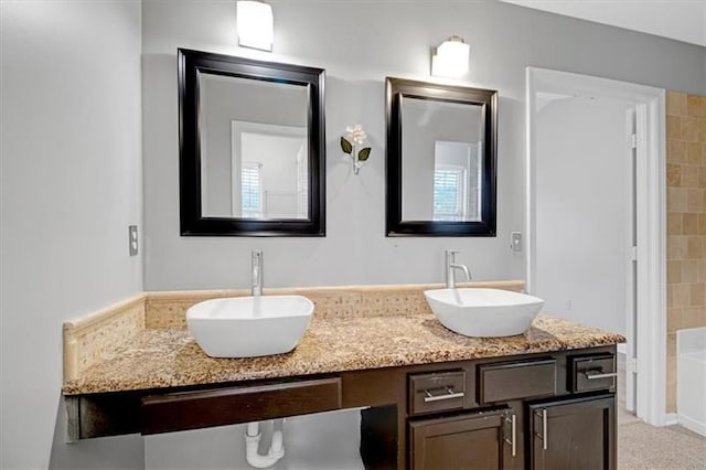 full bathroom with double vanity, a tub to relax in, and a sink