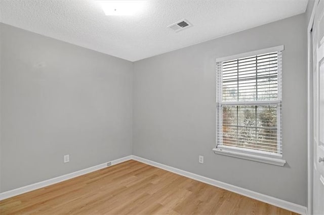 spare room with visible vents, a textured ceiling, light wood-type flooring, and baseboards