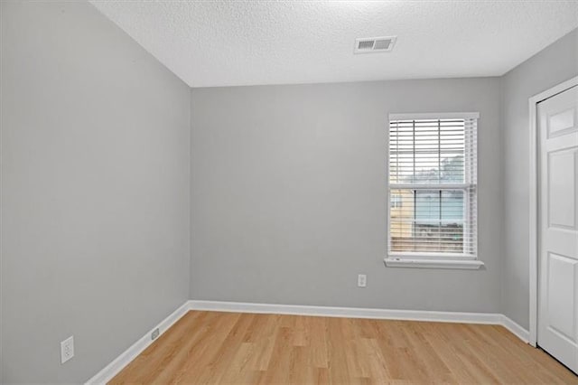 spare room featuring visible vents, baseboards, a textured ceiling, and light wood-style flooring