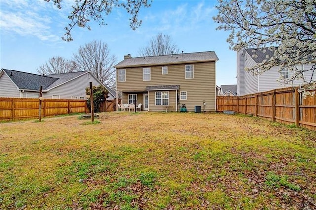 back of property with central AC unit, a lawn, a chimney, and a fenced backyard