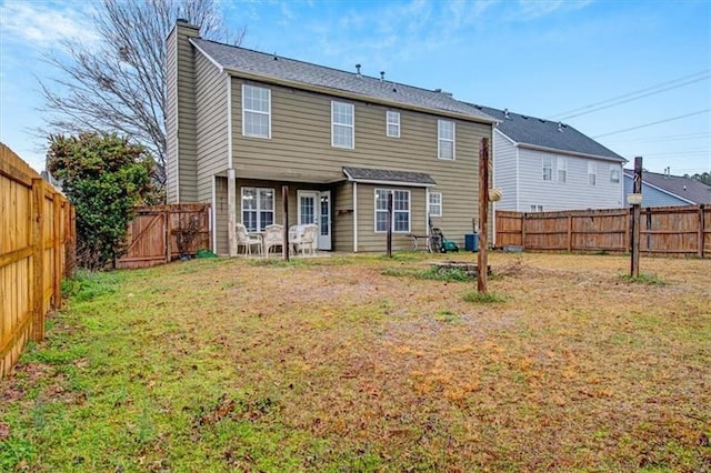 rear view of house featuring a lawn, a chimney, and a fenced backyard