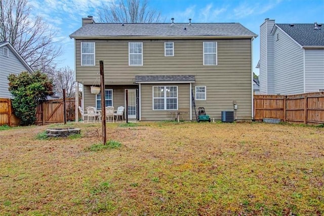 rear view of house with cooling unit, a fenced backyard, a lawn, and a chimney