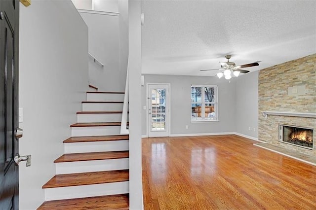 interior space featuring a textured ceiling, wood finished floors, stairway, a fireplace, and ceiling fan