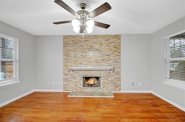 unfurnished living room with a stone fireplace, wood finished floors, baseboards, and ceiling fan