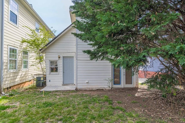 rear view of house with central AC unit and a lawn