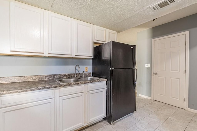 kitchen with white cabinets, light tile patterned flooring, black fridge, and sink