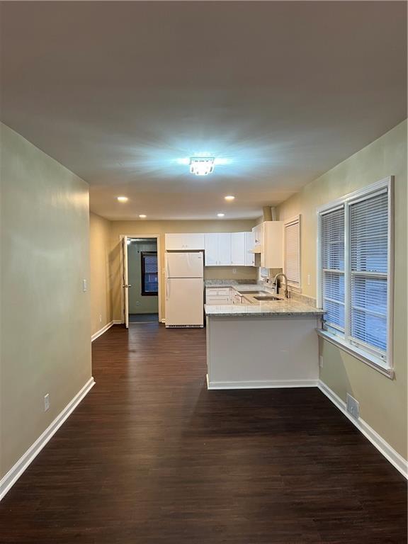 kitchen featuring dark wood-type flooring, light stone countertops, white cabinets, kitchen peninsula, and white fridge