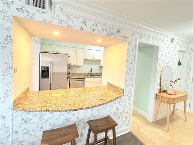 kitchen with kitchen peninsula, white cabinetry, light stone countertops, stainless steel appliances, and ornamental molding