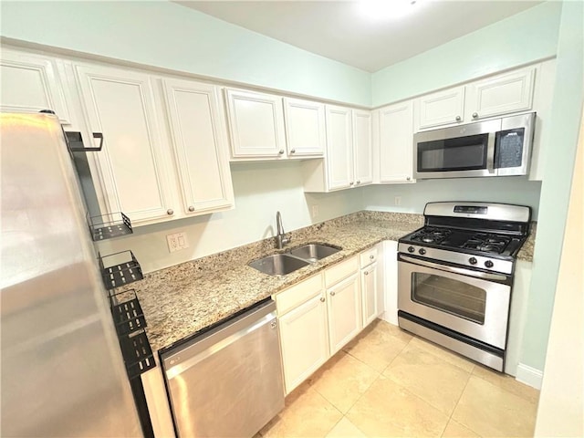 kitchen with appliances with stainless steel finishes, white cabinetry, sink, light stone counters, and light tile patterned floors