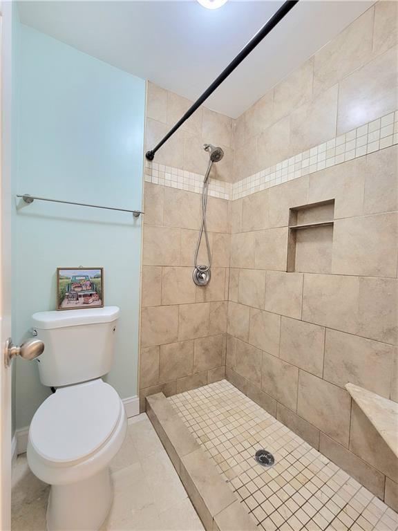 bathroom with tile patterned floors, toilet, and a tile shower