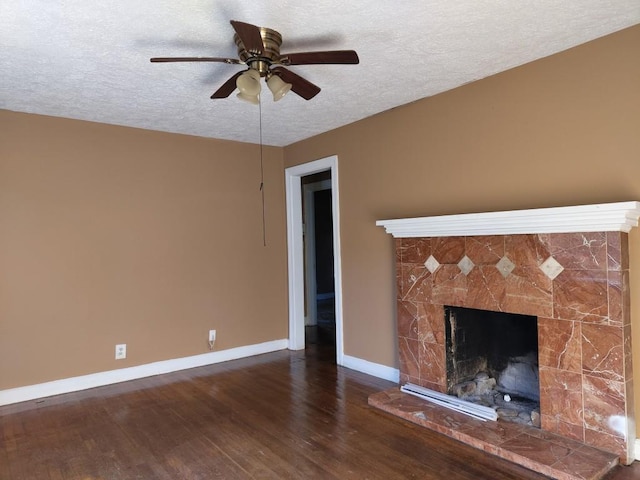 unfurnished living room featuring ceiling fan, dark wood-type flooring, a stone fireplace, and a textured ceiling