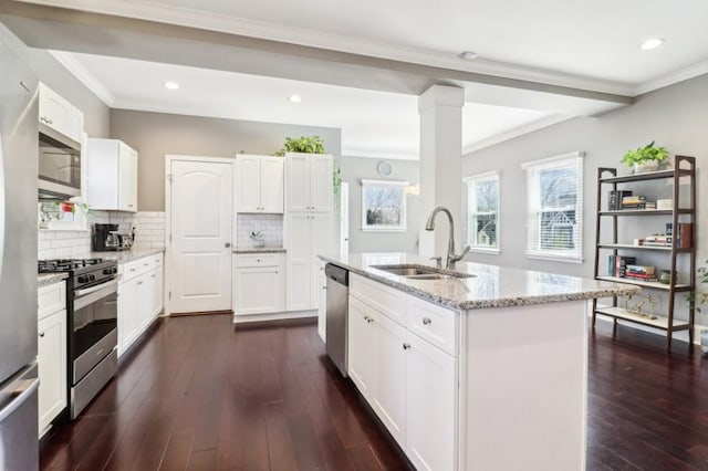 kitchen with sink, appliances with stainless steel finishes, light stone counters, white cabinets, and a center island with sink