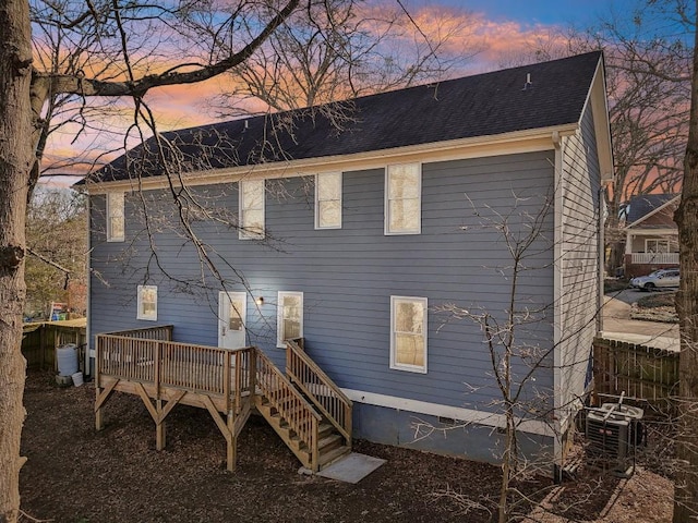 back house at dusk featuring a wooden deck and central AC unit