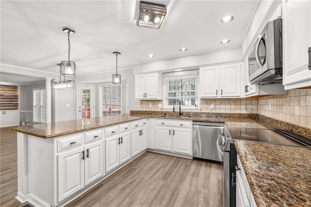 kitchen featuring kitchen peninsula, pendant lighting, stainless steel appliances, tasteful backsplash, and white cabinets