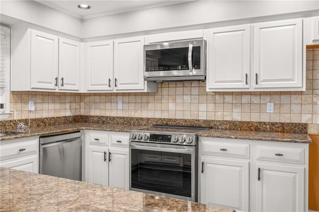 kitchen with stainless steel appliances, white cabinetry, dark stone countertops, and backsplash