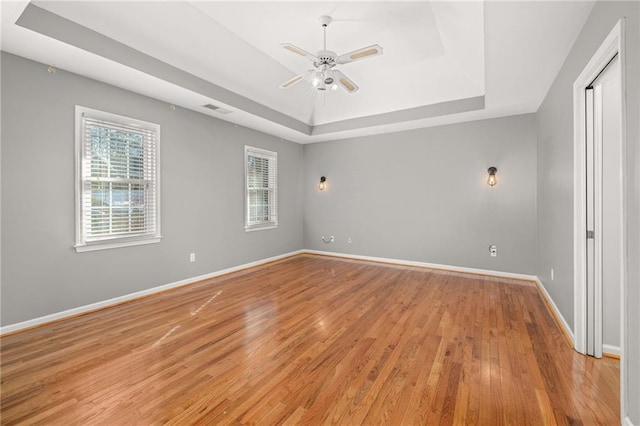 spare room with ceiling fan, light wood-type flooring, and a raised ceiling