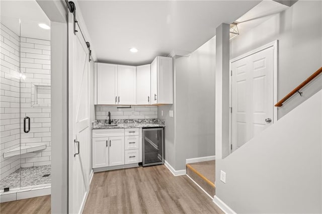 bar featuring sink, white cabinetry, light stone counters, a barn door, and wine cooler