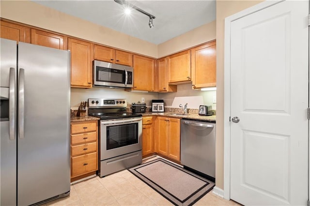 kitchen with sink, light tile patterned floors, stainless steel appliances, and dark stone counters