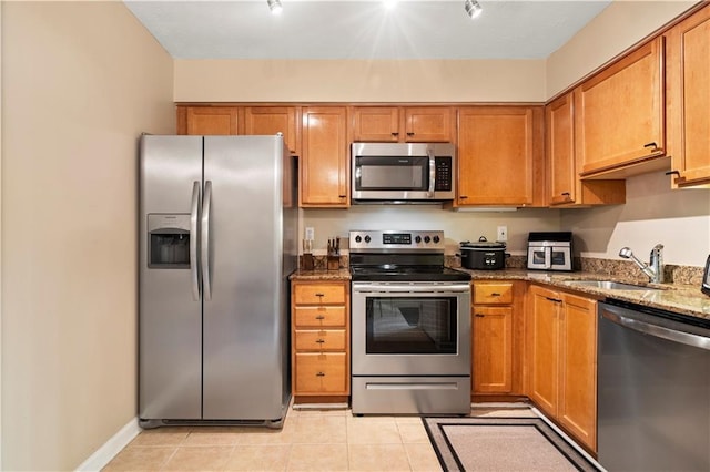 kitchen featuring appliances with stainless steel finishes, rail lighting, sink, dark stone counters, and light tile patterned floors