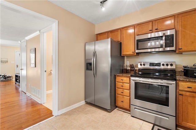 kitchen featuring track lighting, stainless steel appliances, dark stone counters, and light tile patterned flooring