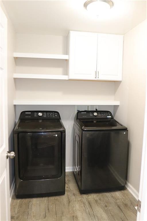 laundry room featuring washing machine and dryer, light hardwood / wood-style flooring, and cabinets