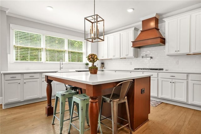 kitchen with custom exhaust hood, a kitchen breakfast bar, light countertops, light wood-style flooring, and a center island