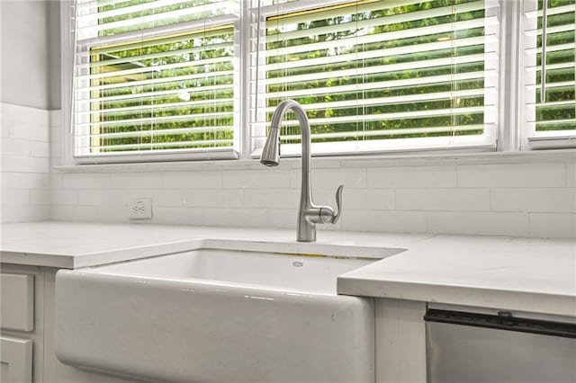 detailed view of a sink, decorative backsplash, and light stone counters
