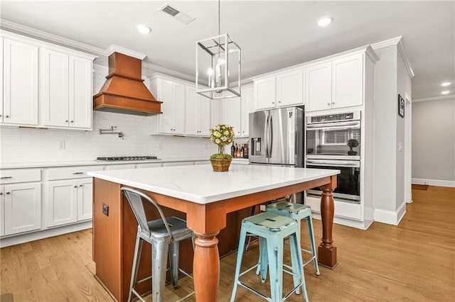 kitchen with appliances with stainless steel finishes, ornamental molding, premium range hood, a kitchen bar, and decorative backsplash