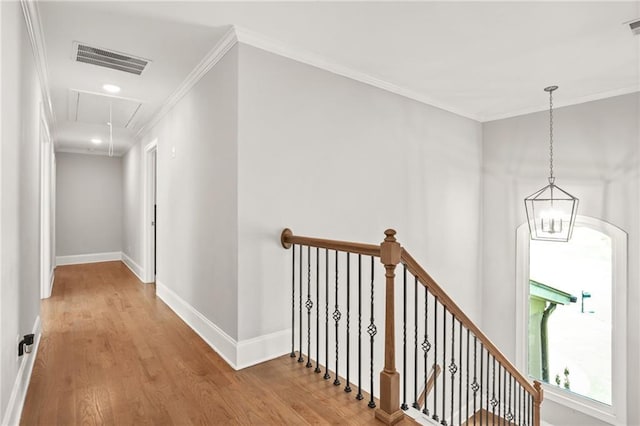 hallway with attic access, an upstairs landing, wood finished floors, ornamental molding, and baseboards