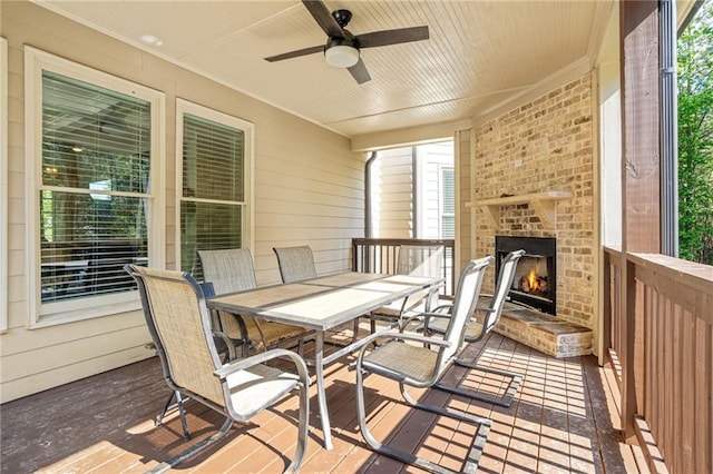 wooden terrace with an outdoor brick fireplace, outdoor dining area, and a ceiling fan