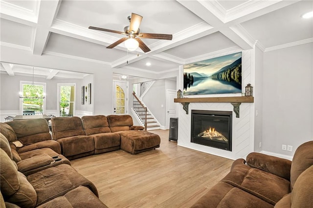 living room with coffered ceiling, light wood-style floors, a fireplace, a ceiling fan, and stairs