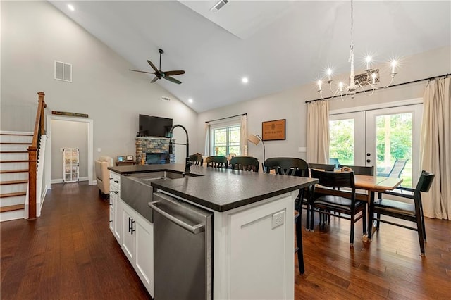 kitchen with white cabinetry, a kitchen bar, a stone fireplace, a kitchen island with sink, and dishwasher