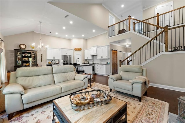 living room featuring a barn door, a chandelier, high vaulted ceiling, and wood-type flooring