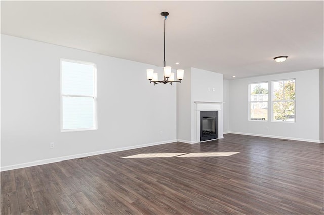 unfurnished living room with an inviting chandelier, a glass covered fireplace, baseboards, and dark wood finished floors