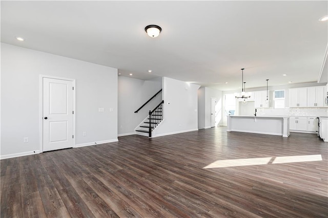 unfurnished living room featuring baseboards, recessed lighting, stairway, dark wood finished floors, and a notable chandelier