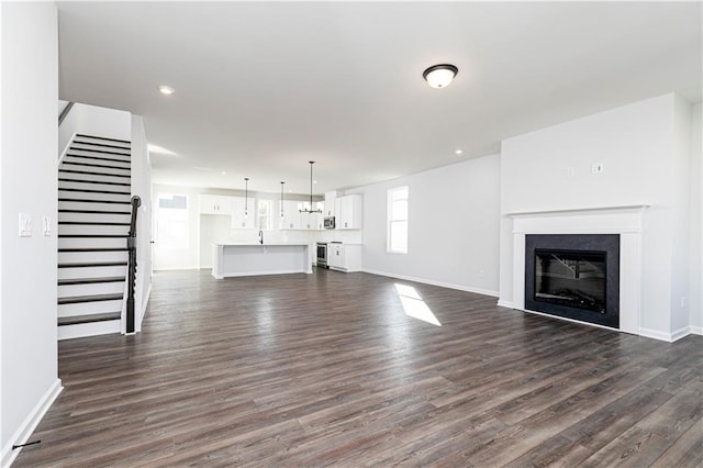 unfurnished living room featuring a glass covered fireplace, baseboards, stairs, and dark wood finished floors